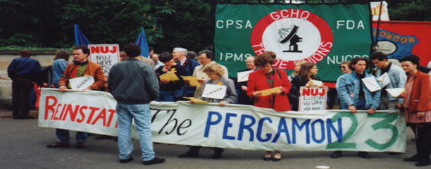 People standing behind a long table with a banner in front of it reading "Reinstate the Pergamon 23".